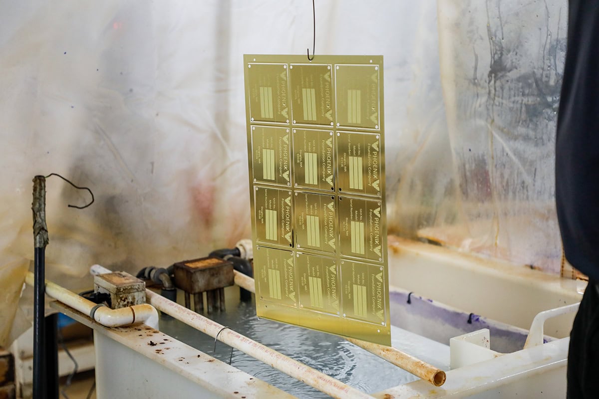 Sheet of gold labels with multiple rectangles hanging above a water bath in a workshop setting.