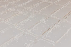 White tiled surface lightly dusted with small salt crystals scattered along the grout lines