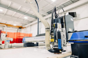 Industrial CNC laser cutting machine with a large flexible exhaust hose in a factory setting.