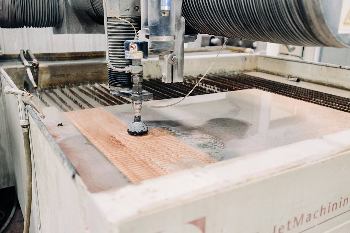 Industrial waterjet cutter slicing a copper sheet, nozzle directing a high-pressure jet onto the metal surface.