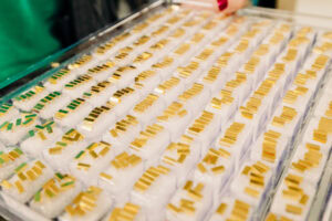 Rows of gold-plated rectangular components lined up in foam trays on a production line.