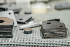 Several rectangular steel weight plates stacked on a textured workshop bench, with a small round cap nearby.