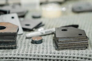Close-up of rusted metal blocks and small spacers on a textured workshop surface, suggesting metalworking parts at a bench they sit on.