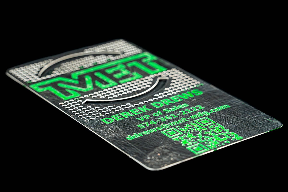 Metal business card with a green raised 'LEVEL' logo, circular arc design, contact details etched in green, and a QR code on a dark background