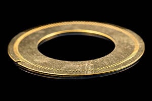 Close-up of a gold circular ring with evenly spaced tiny holes along the inner edge, set against a black background.