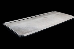 Close-up of a long, flat metal blade with fine serrated edges on the sides, set against a black background (precision cutting tool).
