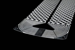 Close-up of a curved, perforated metal strip with a diamond lattice pattern on a black background, showing rounded corner holes.