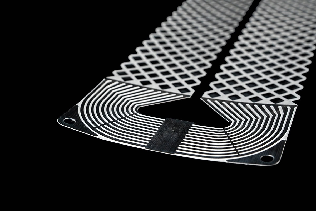 Close-up of a curved, perforated metal strip with a diamond lattice pattern on a black background, showing rounded corner holes.