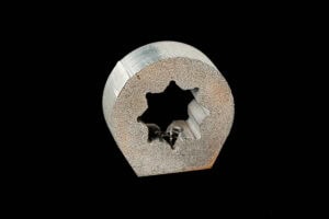 Cross-section of a gray metal tube with a jagged star-shaped inner hole on a black background.