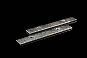 Two flat silver metal strips with round holes rest on a black background.