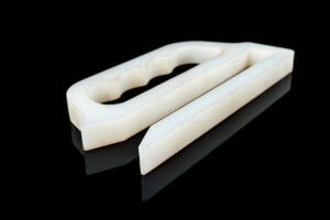 Two white plastic pieces on a black background: a wedge-shaped block and a second piece with a curved, hollow handle-like cutout.