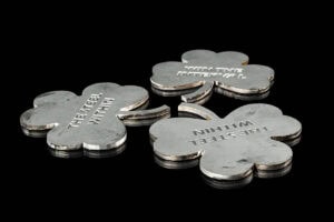 Four metallic four-leaf-clover tokens with engravings on a black reflective surface, arranged in a small cluster.