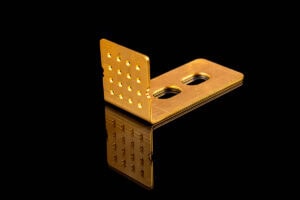 Gold-plated metal L-shaped connector with a perforated vertical plate and two oval holes on a black reflective surface.