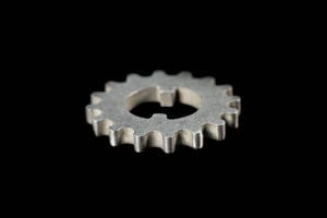 Single silver metal gear cog on a black background, viewed from the side with rounded teeth visible.