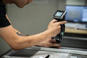 Man using a handheld barcode scanner to scan a form on a desk, close to the paper document on a metal counter.