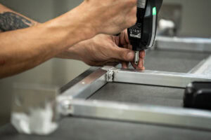 Close-up of a person drilling a metal frame with a power drill during assembly of the frame.