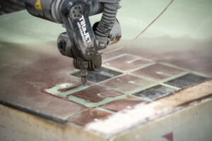 Close-up of a waterjet cutter cutting a metal sheet with a grid pattern.