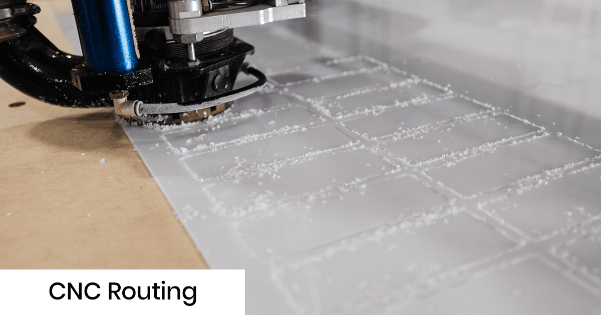 CNC router cutting a white acrylic sheet, creating plastic chips around the cutting bit