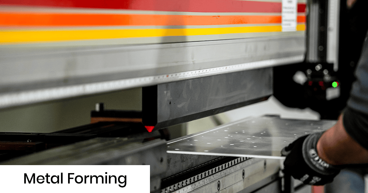 Sheet metal being formed by a press brake in a workshop, worker wearing gloves guiding the metal sheet