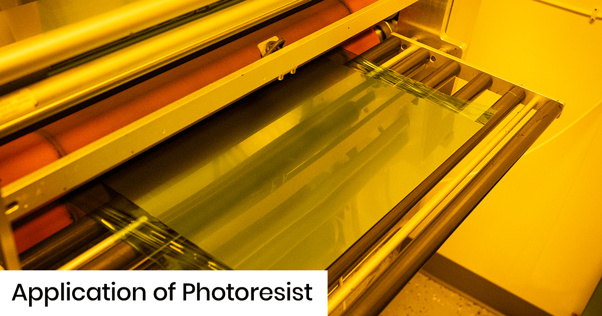 Glass sheet in a photoresist coating machine with rollers, under yellow lighting, showing the resist application process.