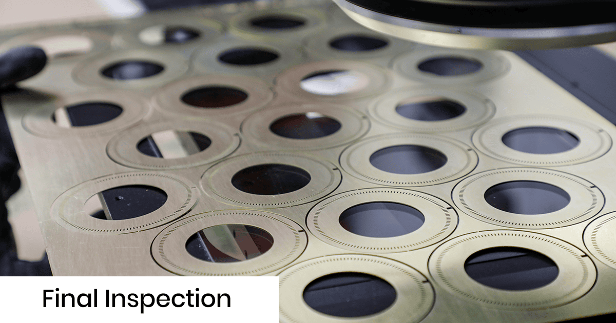 Final inspection of a metal sheet with circular cutouts; rows of holes in brass-colored sheet.